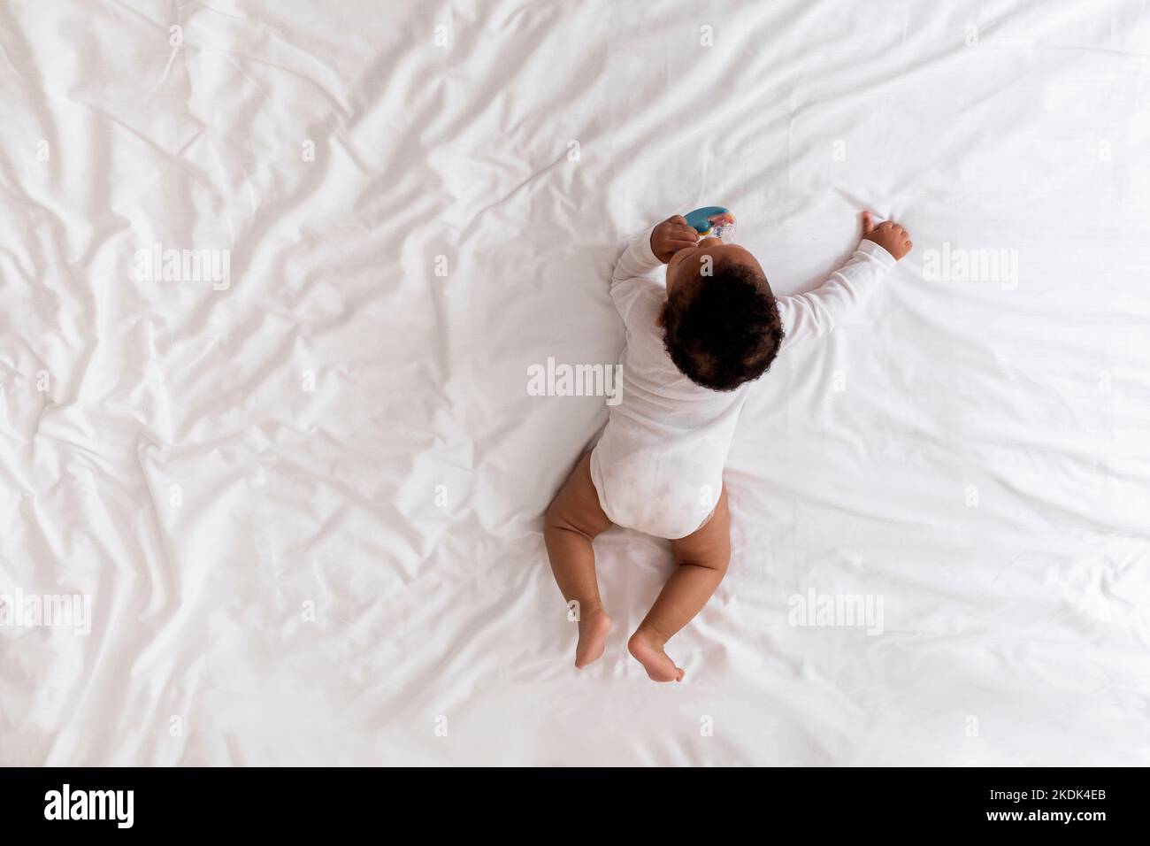 Little Black Baby Crawling On Bed And Playing With His Rattle Toy Stock Photo