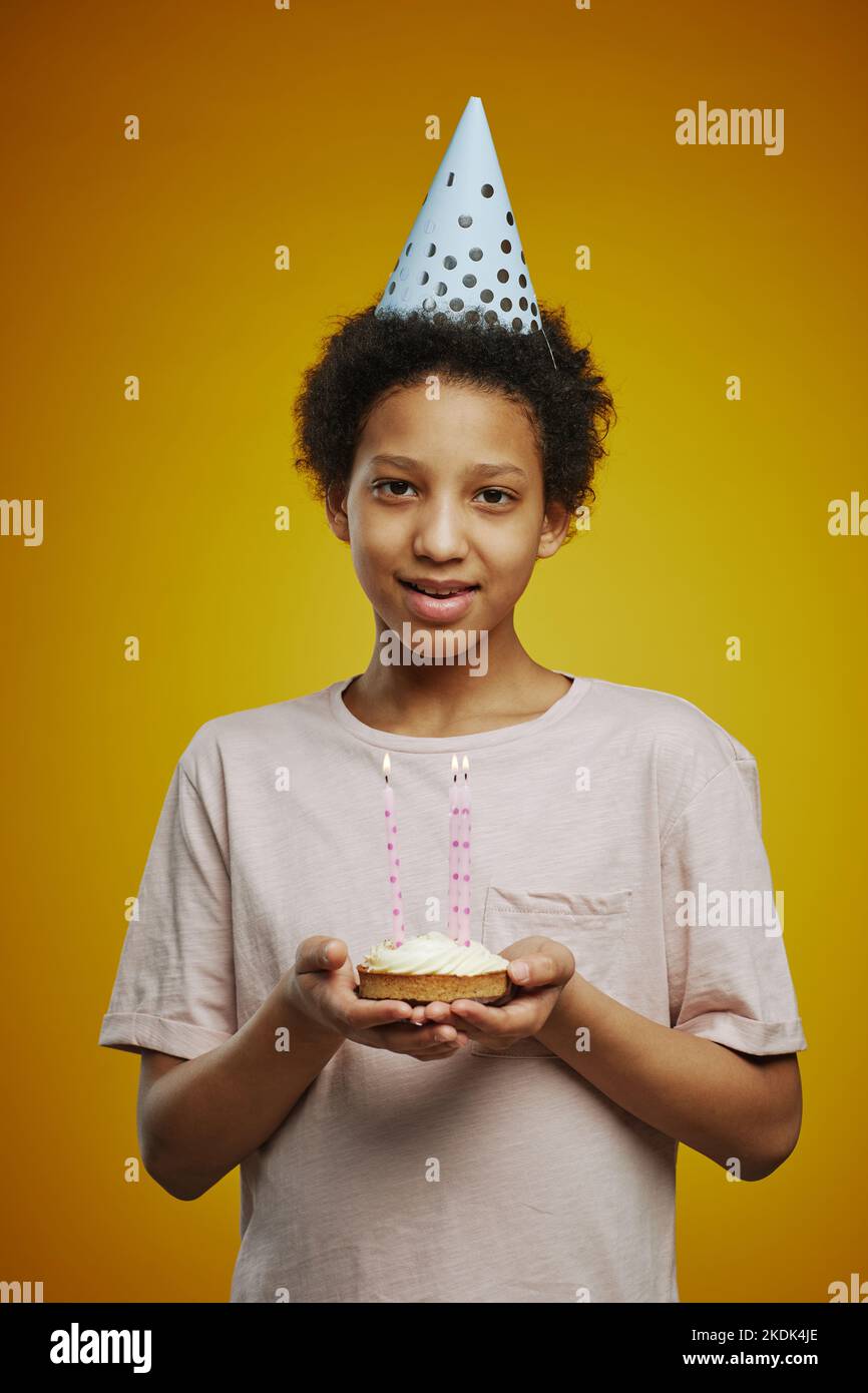 Smiling adolescent girl in white t-shirt and cap holding small birthday