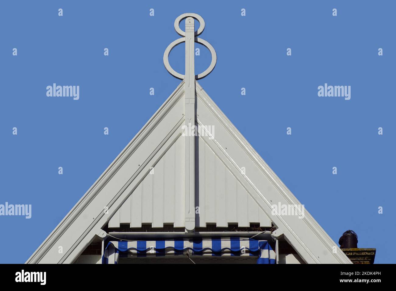 Top of a white wooden facade with a finial or hip knob as a decorative feature. Roof spire of a Dutch house.Blue sky. Canopy top. Stock Photo