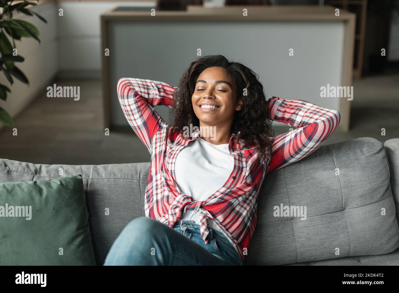 Smiling pretty black young woman with closed eyes rest alone on sofa in minimalist living room interior Stock Photo