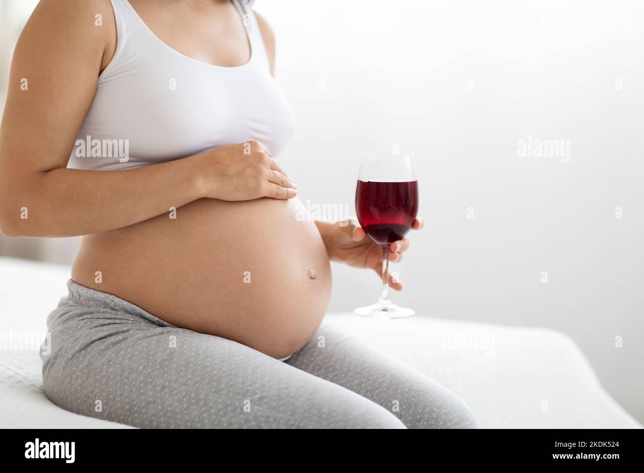 Unrecognizable pregnant woman holding glass of red wine, cropped Stock Photo