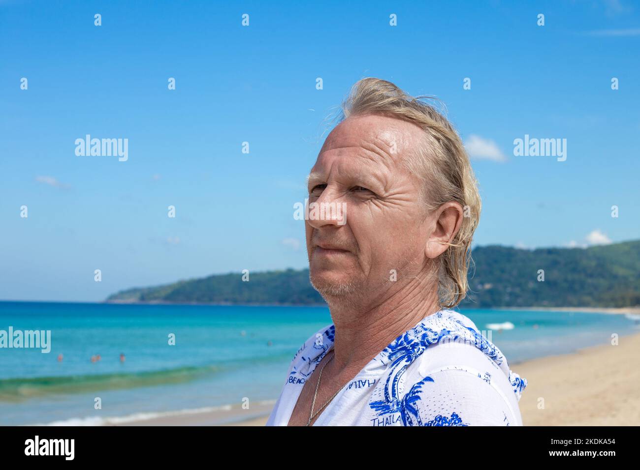 A fair haired adult male tourist looks into the distance on the seashore on a sunny day. Travel and tourism. Stock Photo