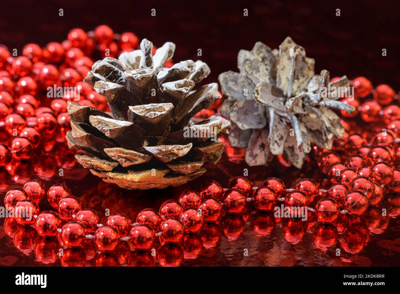Christmas decoration with two pine cones and a red beaded garland on a red shiny background. Stock Photo