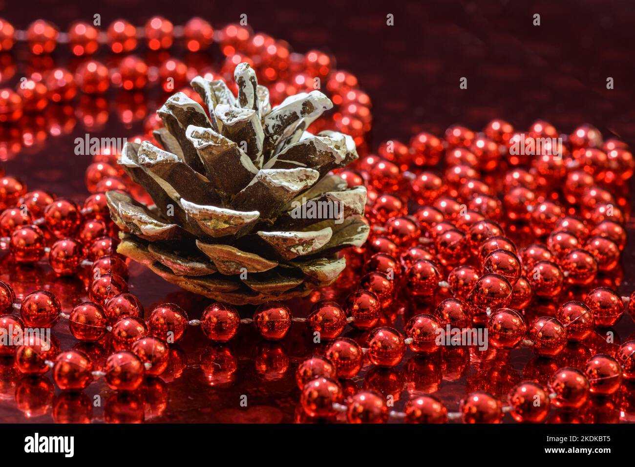 Christmas decoration with a pine cone and a red beaded garland on a red shiny background. Stock Photo