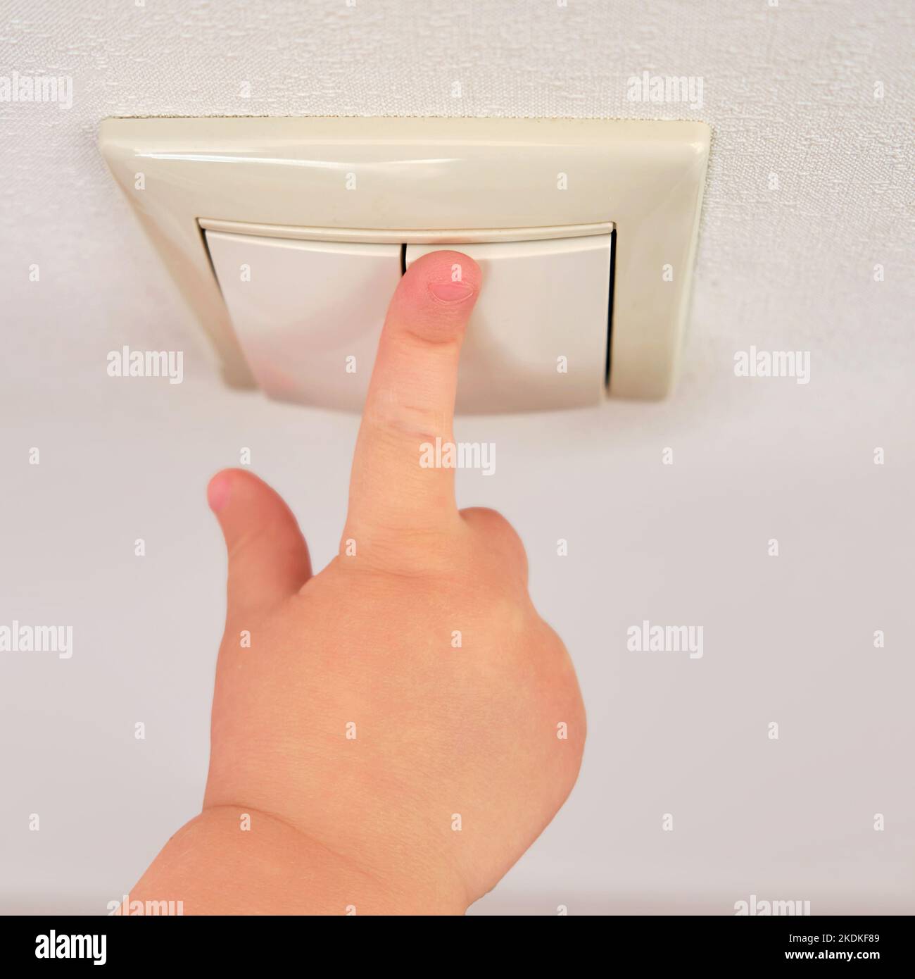 Toddler baby reaches for the light switch, child hand turns on the lamp closeup. White light