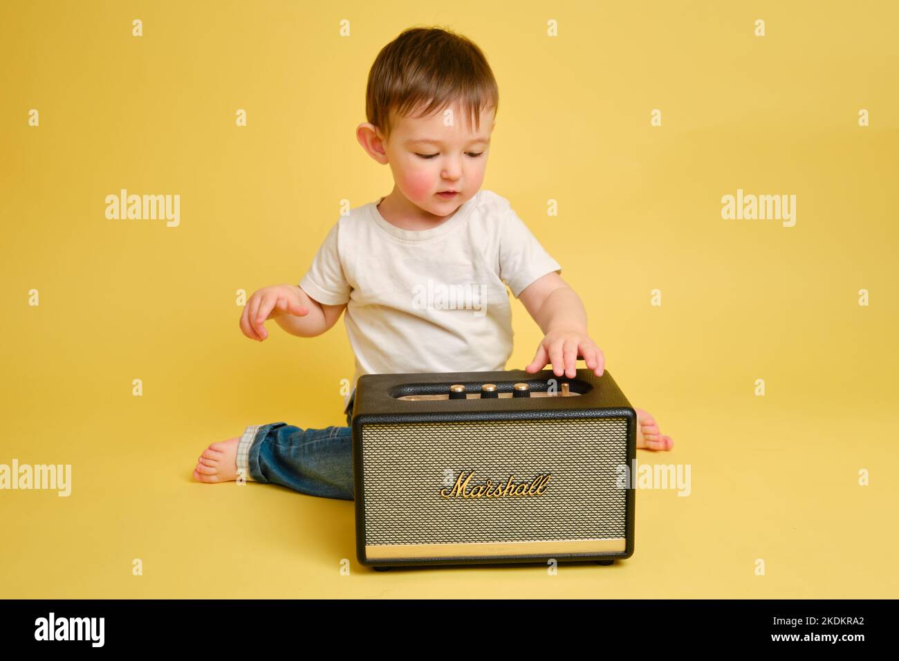 Toddler baby plays with a wireless music speaker Marshall on a studio