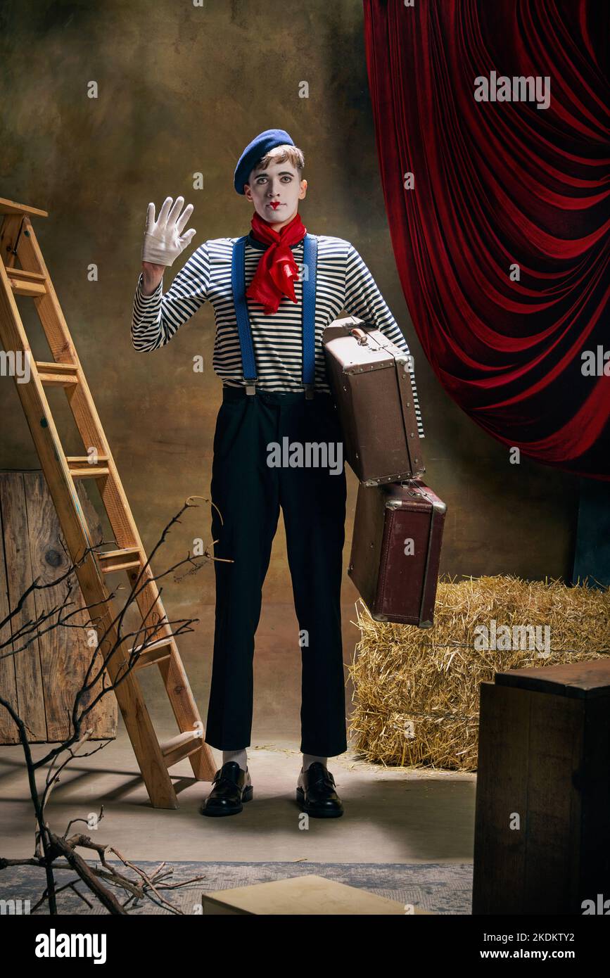 Vintage portrait of male mime artist expressing sadness and loneliness over dark retro circus backstage background. Concept of emotions, art, fashion Stock Photo