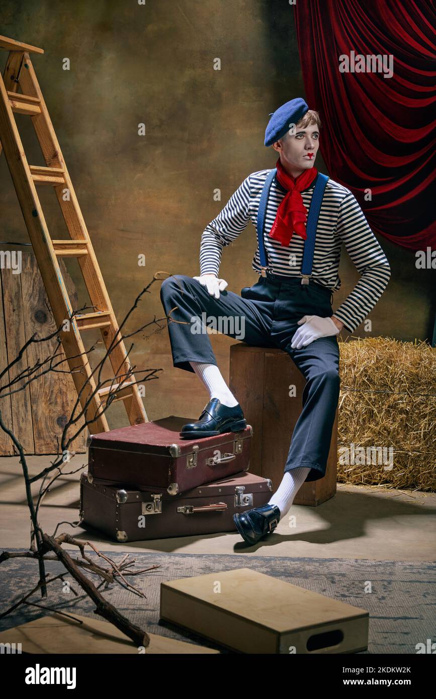 Vintage portrait of male mime artist expressing sadness and loneliness over dark retro circus backstage background. Concept of emotions, art, fashion Stock Photo