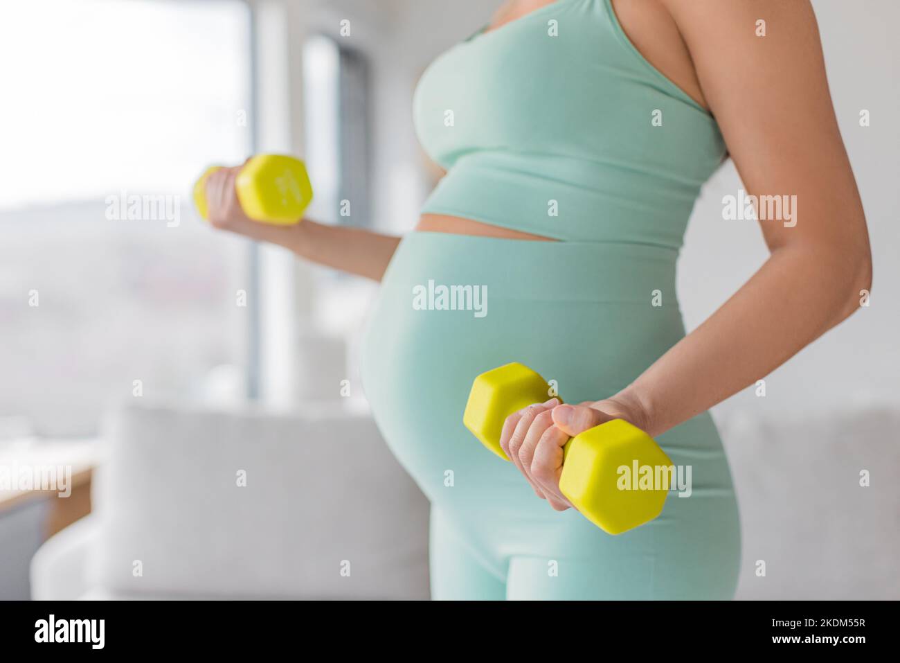 Pregnant woman prenatal training at home doing fitness strength training exercise with dumbbell weights. Body workout arm curls closeup of belly and Stock Photo