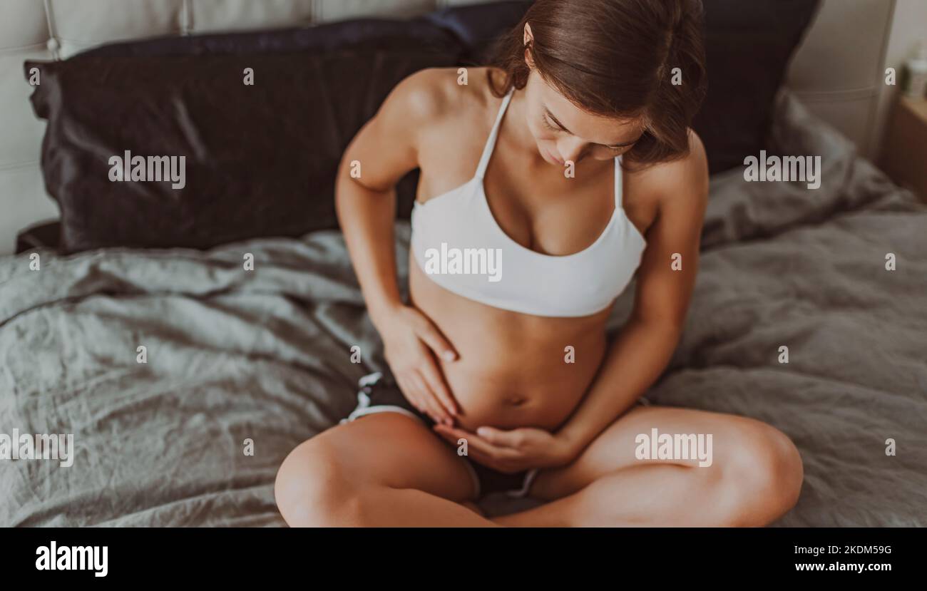 Pregnancy belly stretch marks and black line. Pregnant woman caressing holding stomach during first trimester. Skincare body care health concept Stock Photo