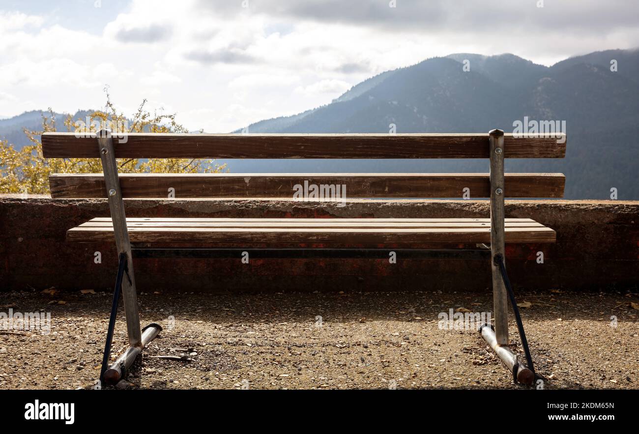 Empty wooden bench, mountain view, cloudy sky background. Back view of lonely bench in countryside, Autumn Stock Photo