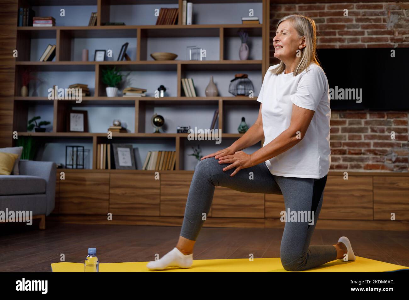 Grayhaired mature woman doing gymnastics and yoga at home and gets a