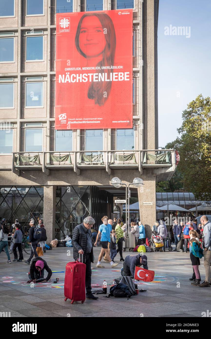 poster of Caritas on the façade of the Domforum emphasises charity, in front of it a pavement painter has put up a Turkish flag, Cologne, Germany. Pla Stock Photo