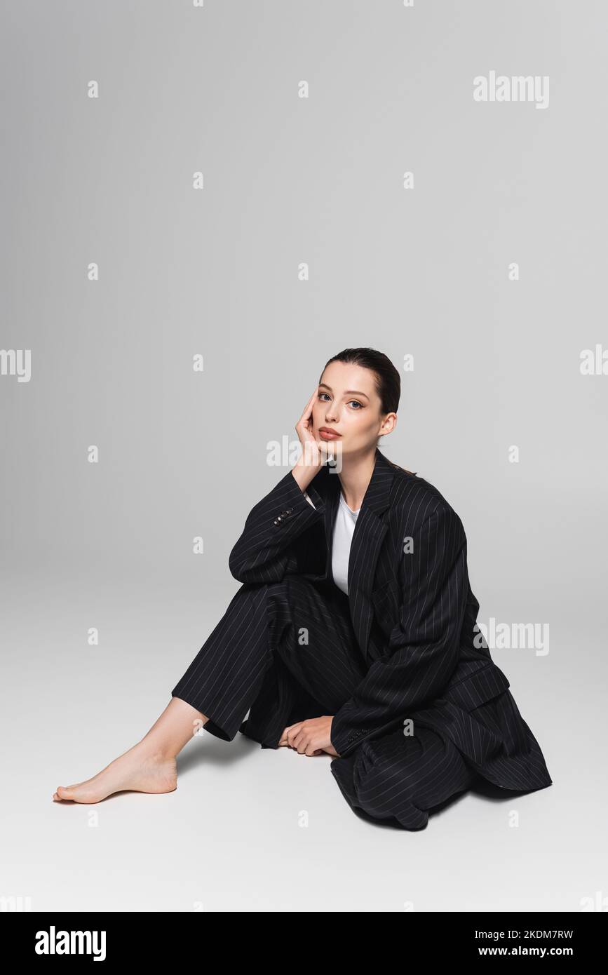 Stylish barefoot model in suit sitting on grey background Stock Photo