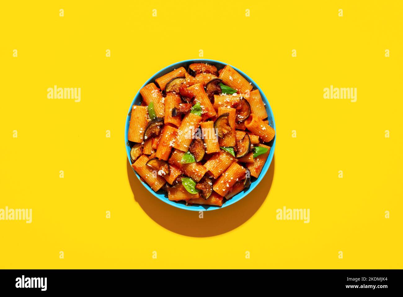 Italian dish, pasta with deep-fried eggplant, top view on a yellow-colored table. Pasta Alla Norma plate minimalist on a colorful background in bright Stock Photo