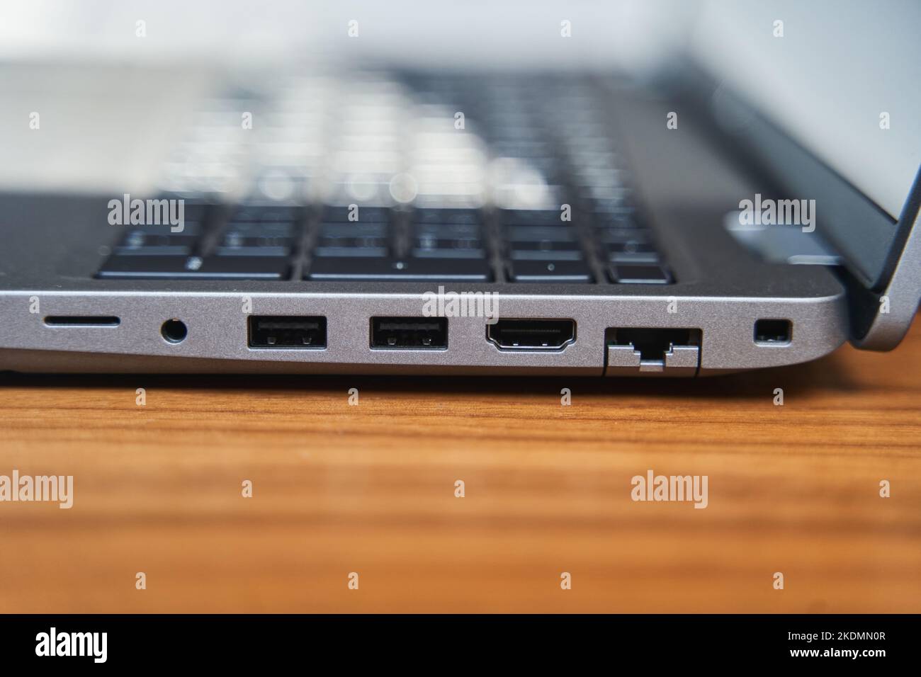 Side view of a gray laptop keyboard on a wooden table. USB ports on a