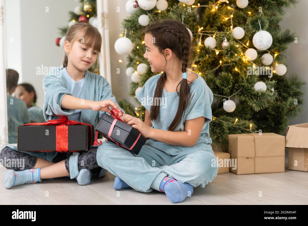 Two little girls open Christmas present under the Christmas tree Stock Open Christmas Present