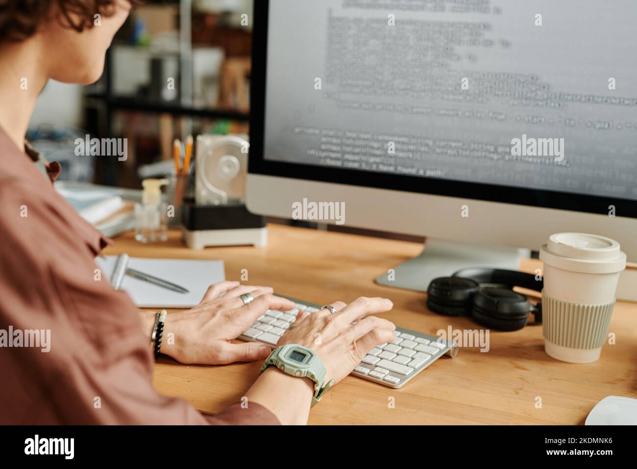 Hands of young female programmer typing on computer keyboard while decoding data on computer screen by workplace in office Stock Photo