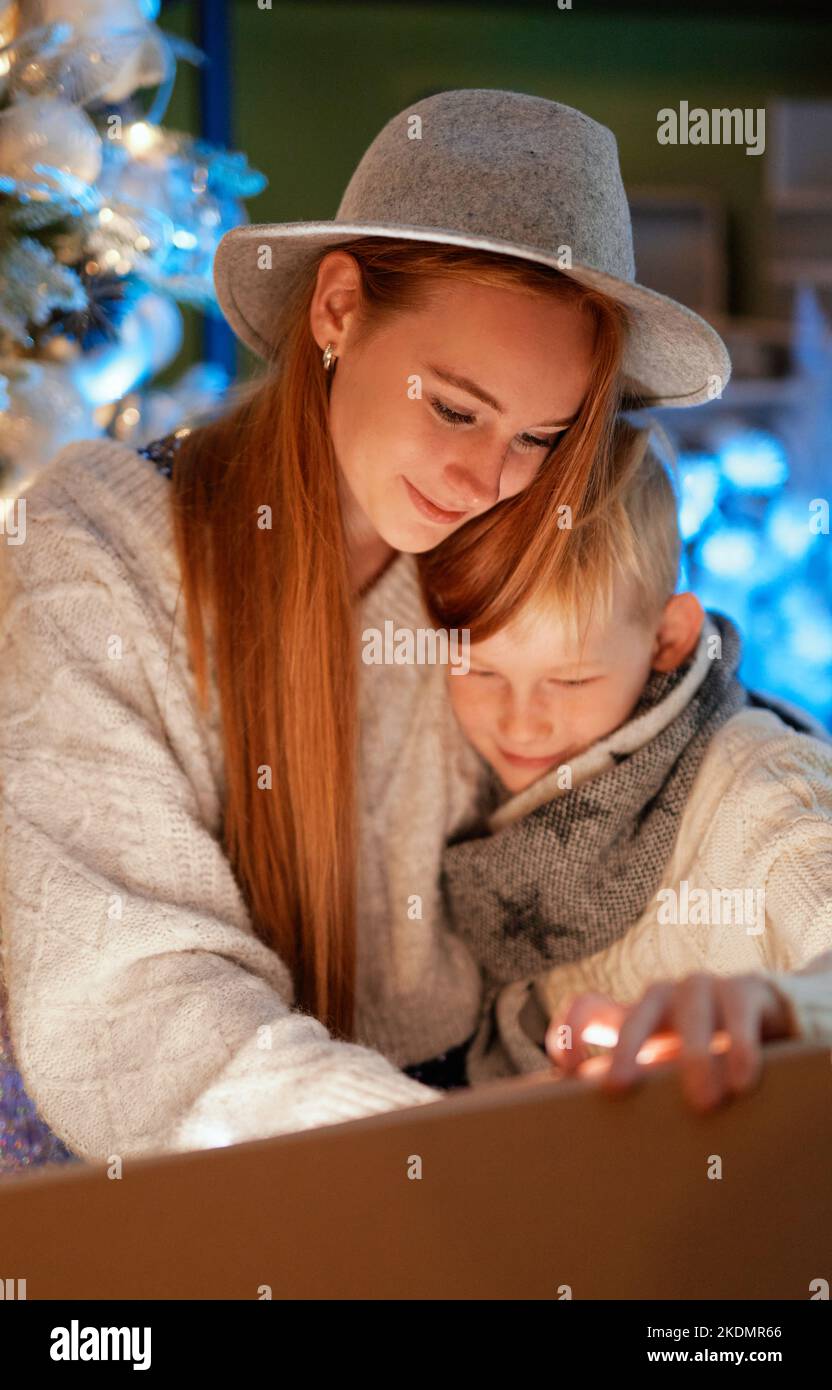 Happy emotions, laughing while opening a present. Christmas 2023: Adorable brother and sister opens Christmas gift at home with xmas tree on background. High quality vertical image Stock Photo