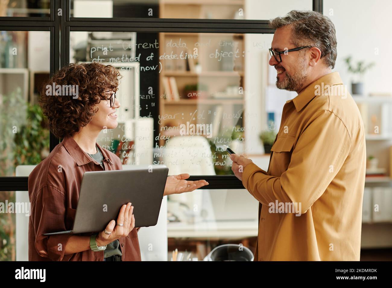 Two happy employees discussing working points by transparent board with notes while brainstorming and expressing their opinions Stock Photo