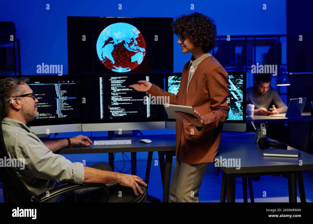 Young confident female programmer making report to mature male colleague while pointing at computer screen with coded data Stock Photo