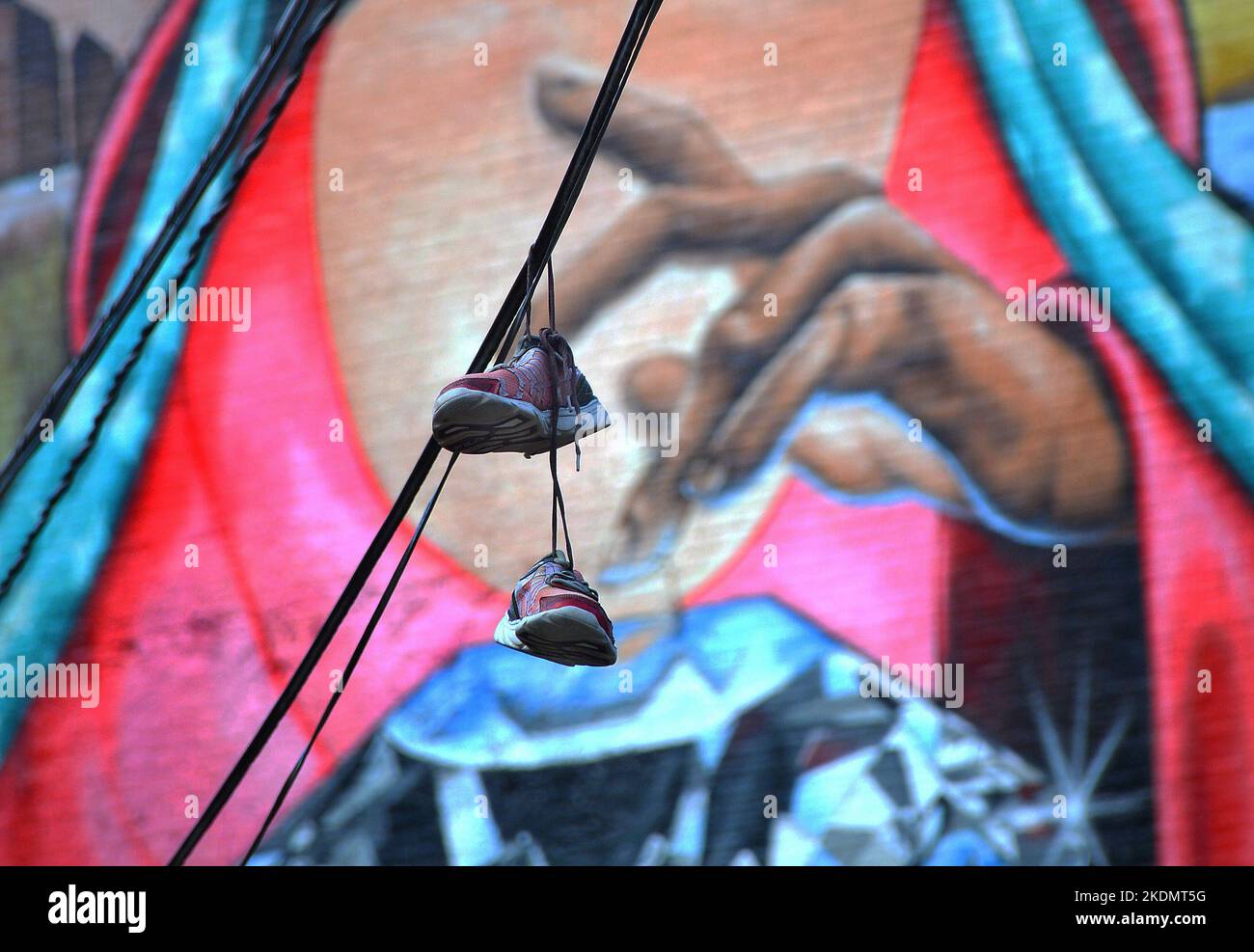 A pair of sneakers hanging on a power line in front of a mural on the