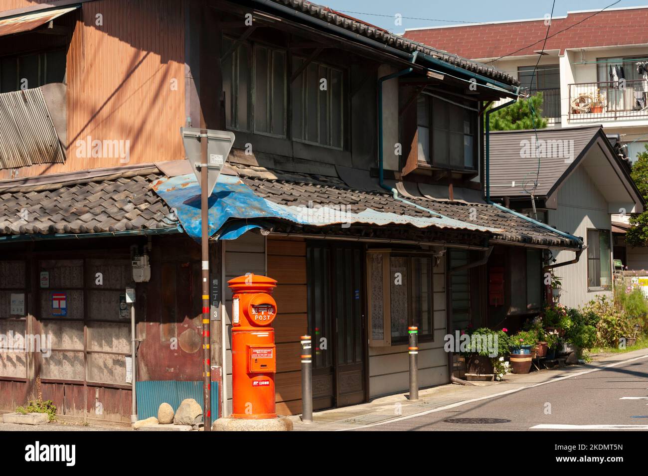 A pillar box post box stands at the corner of a traditional Japanese building on a backstreet in Matsumoto, Nagano, Japan. Stock Photo