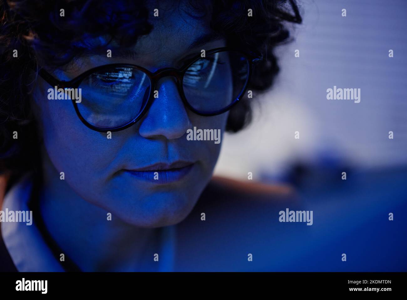 Selective focus of face of serious businesswoman in eyeglasses sitting in front of computer late at night in office and working overtime Stock Photo