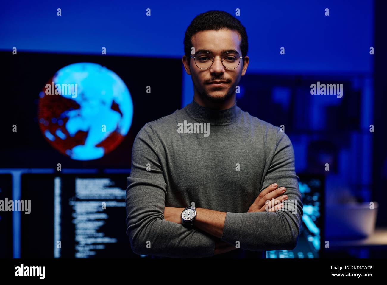 Young modern programmer of huge IT company or corporation keeping his arms crossed on chest while looking at camera in server room Stock Photo