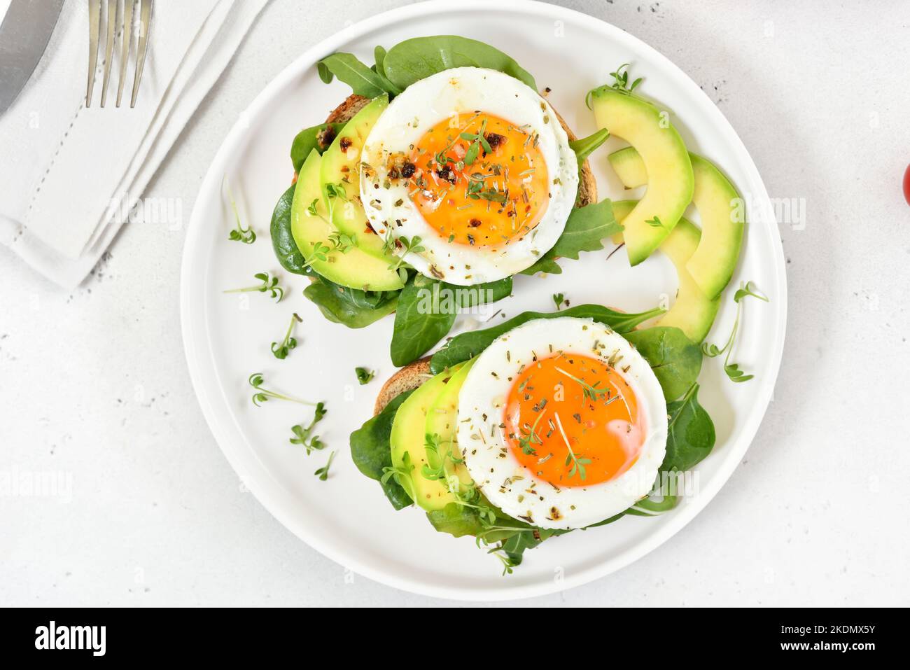 Bread with fried eggs, avocado and greens over light stone background.  Healthy breakfast. Top view, flat lay Stock Photo