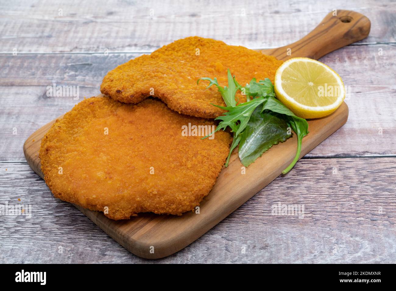 Two Wiener schnitzel placed on a serving board with lemon and garnish Stock Photo