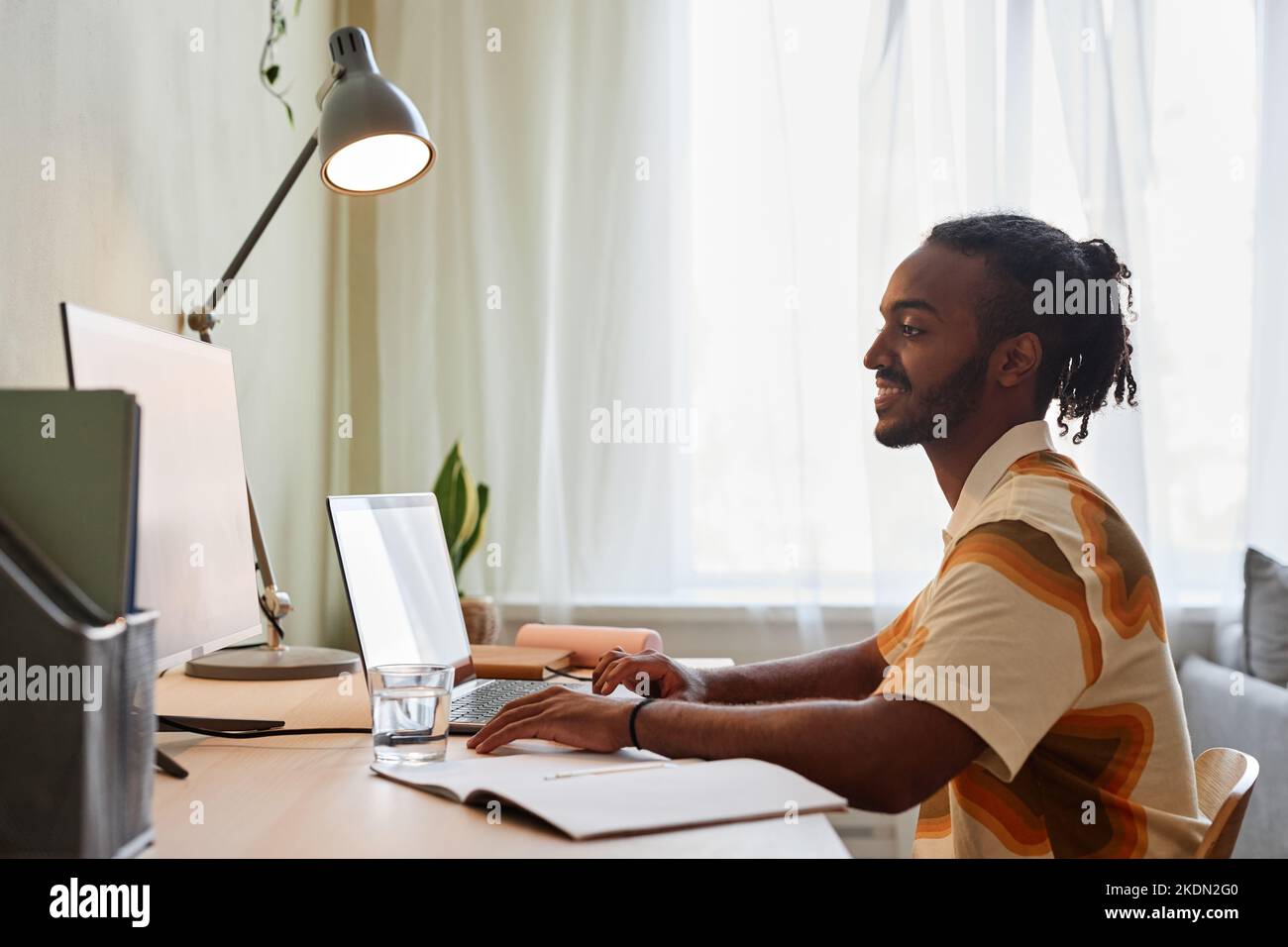 Side view portrait of creative black man smiling during online meeting with team at home office, copy space Stock Photo