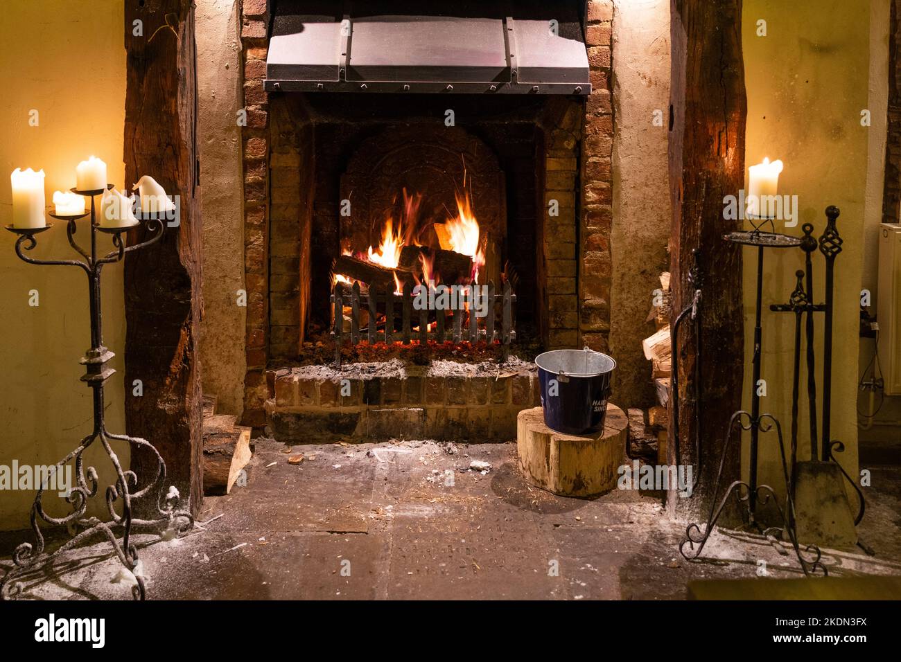 A fire blazing in a traditional fireplace with candles alight on ornate candlesticks in the Millstone restaurant at Bartons Mill, Basingstoke, UK Stock Photo
