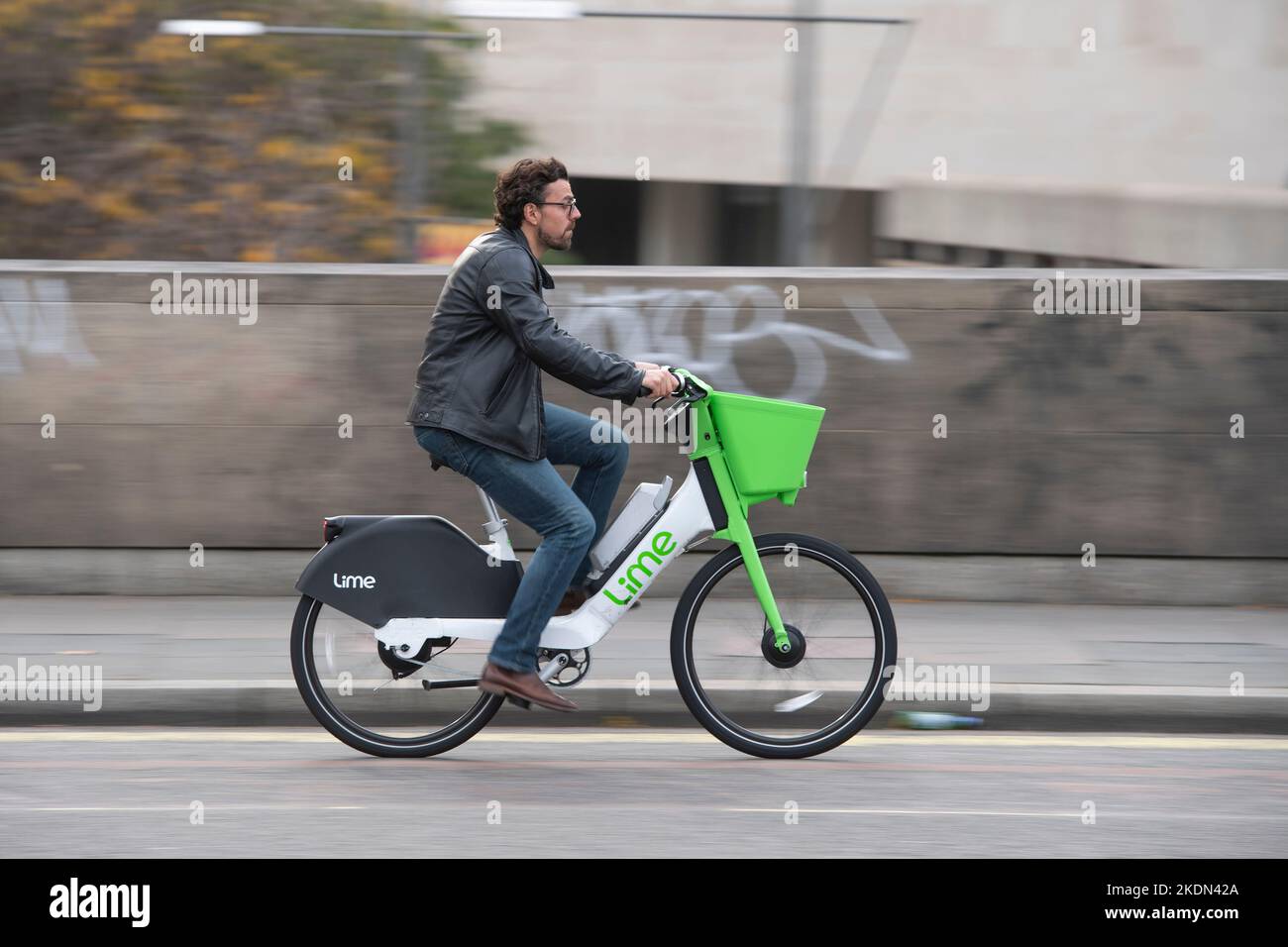 A man riding a Lime electric hire bike on Waterloo Bridge, London, UK