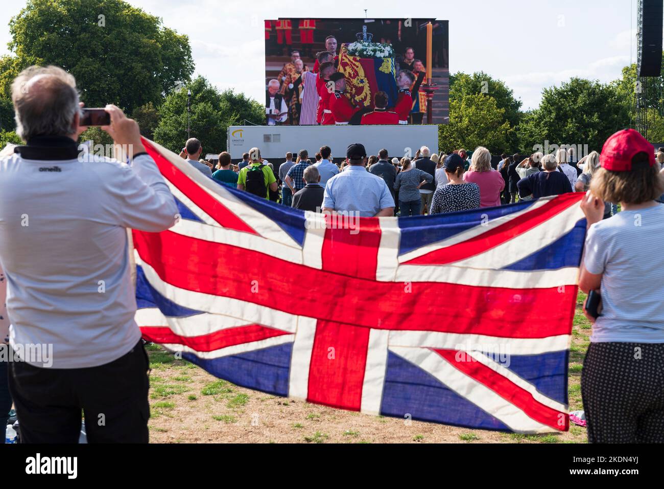 A couple holding a Union Jack flag as they watch the live broadcast of Her Majesty the Queen's coffin being taken by military procession from Buckingh Stock Photo