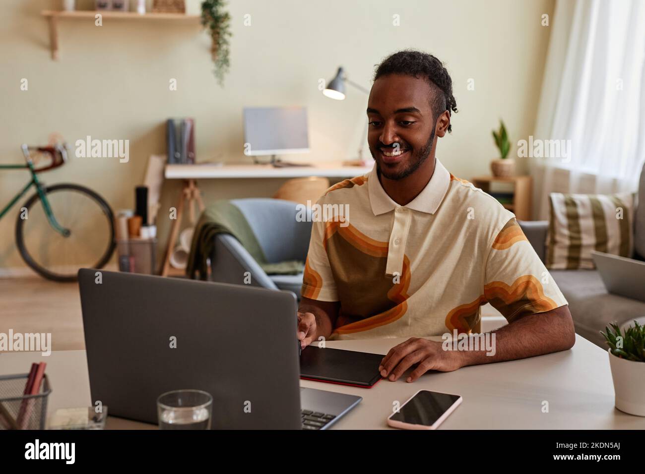 Portrait of smiling black man using pen tablet at home office workplace for digital design or photo editing Stock Photo
