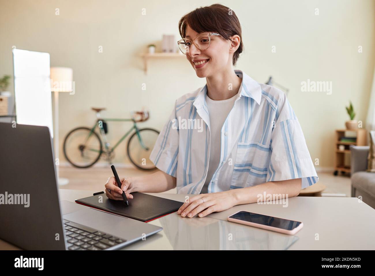 Portrait of smiling young woman using pen tablet at home office workplace for digital design or photo editing Stock Photo