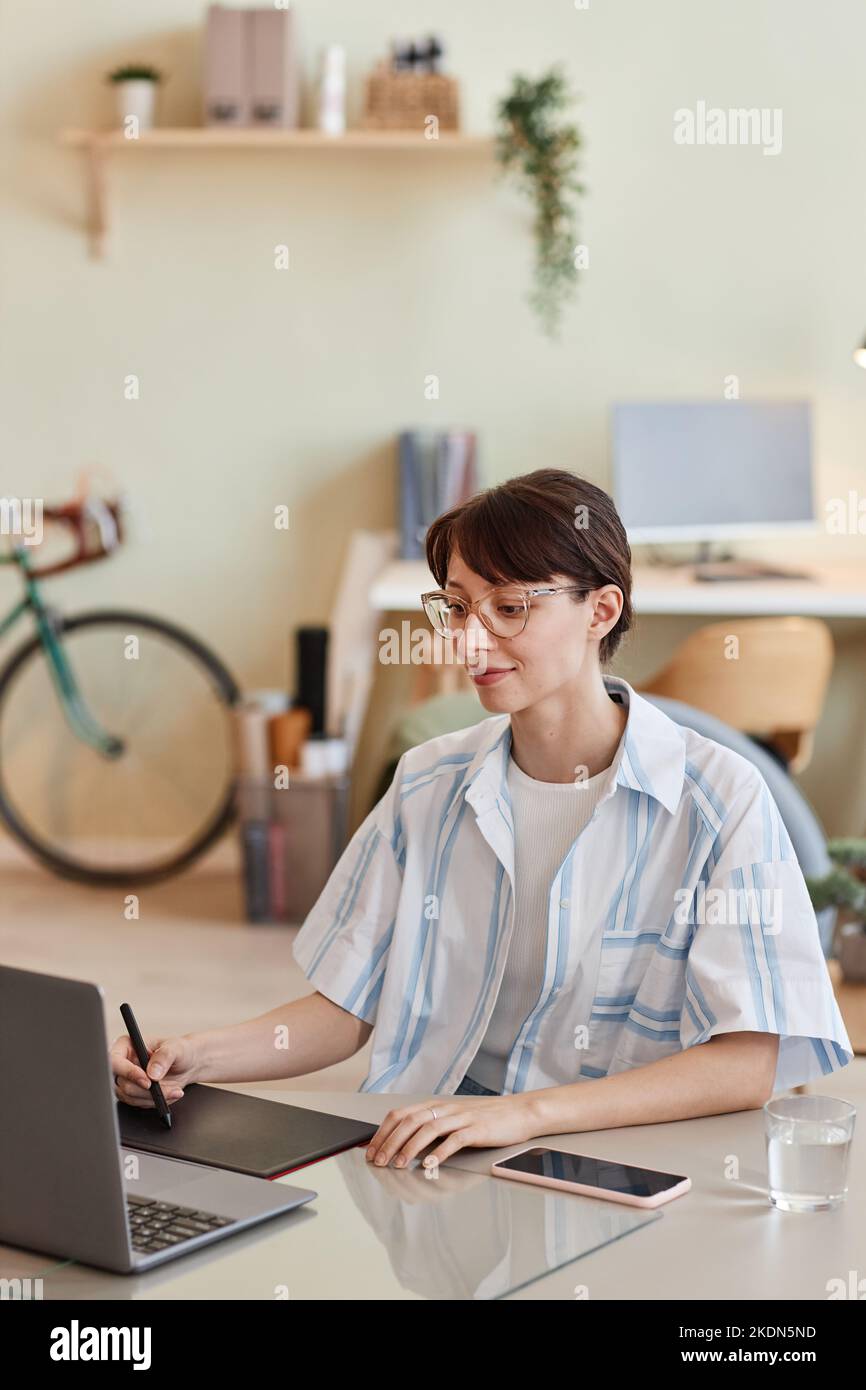 Vertical portrait of young woman using pen tablet at home office workplace for digital design or photo editing Stock Photo