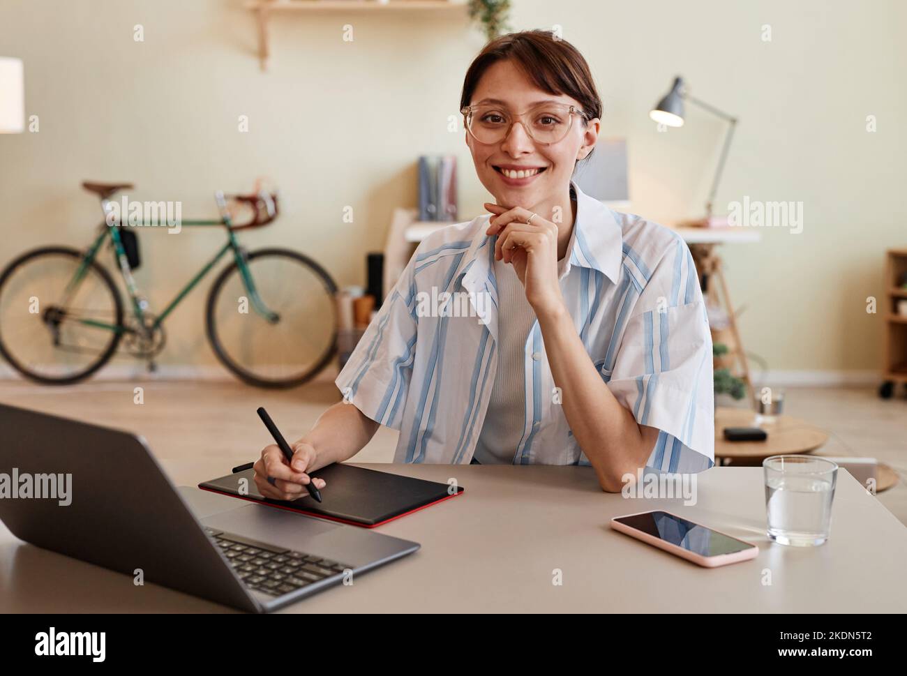 Portrait of young female designer smiling at camera and using pen tablet at home office workplace Stock Photo