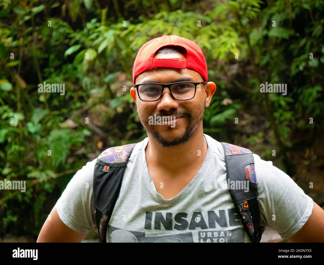 Envigado, Antioquia, Colombia - February 27 2020: Brown Man with Glasses Wears a Red Cap and Smiles at the Camera in the Middle of Nature Stock Photo