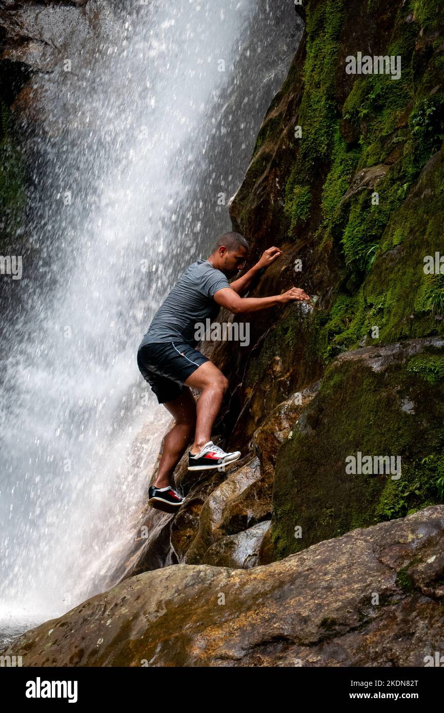 Envigado, Antioquia, Colombia - February 27 2020: Brown Man is Climbing the Rocks next to the Waterfall Stock Photo