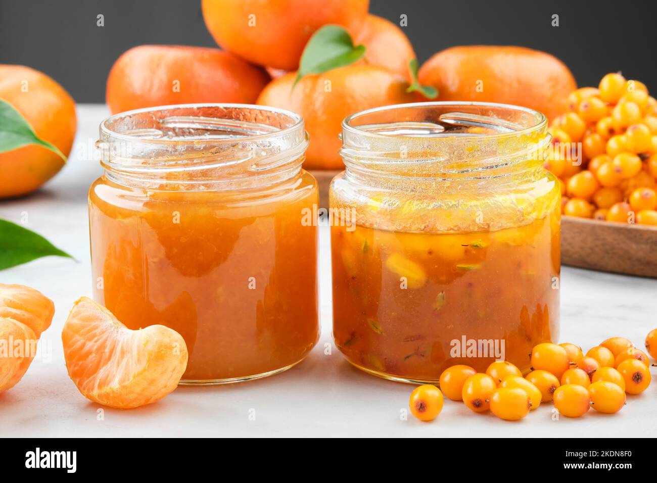 Jars of healthy sea buckthorn and tangerine jam. Plate of sea buckthorn berries and mandarin oranges fruits on background. Stock Photo