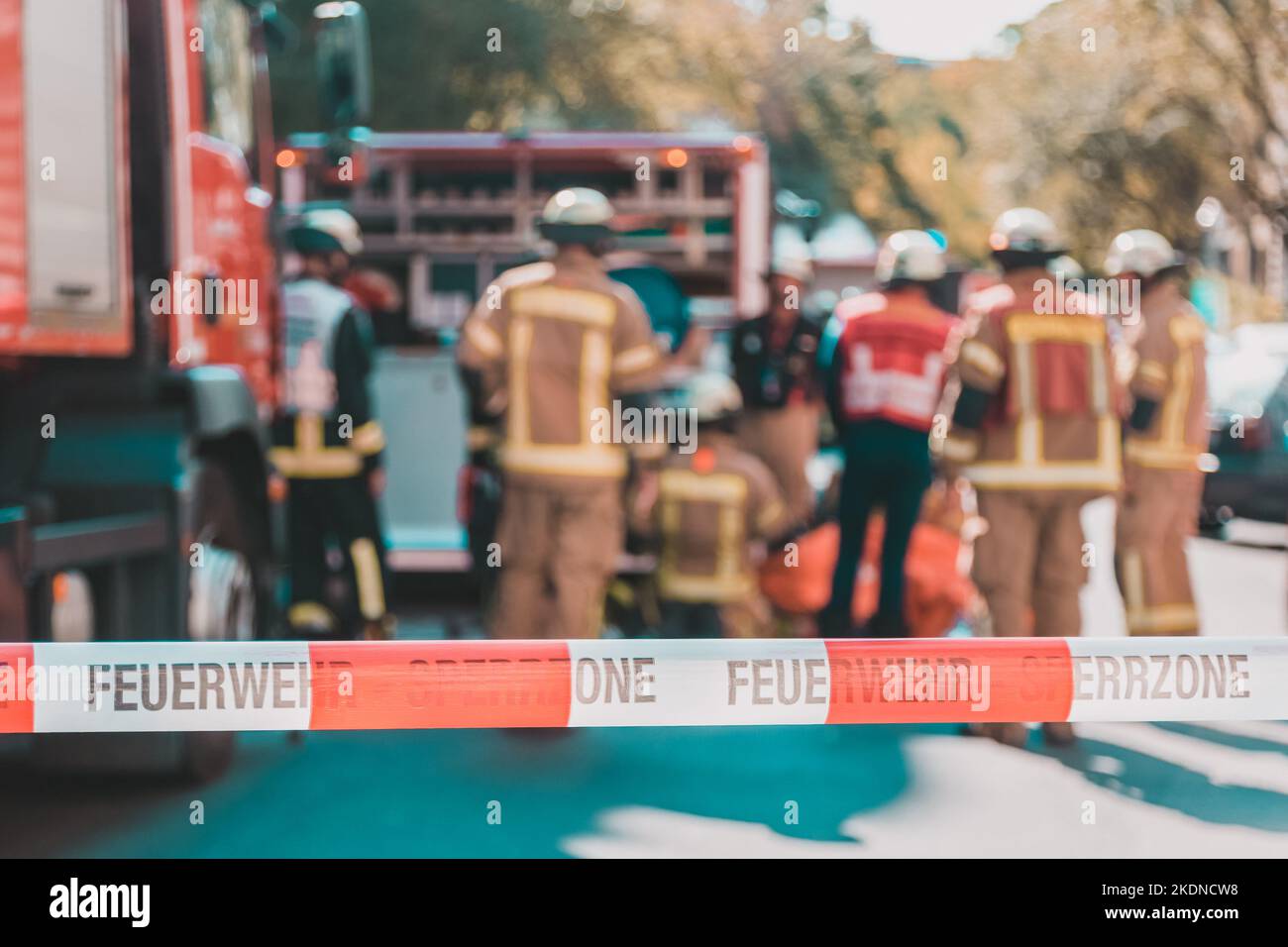 Team of blured firefighters by firetruck on protected accident site. Focus on red and white security band. Stock Photo