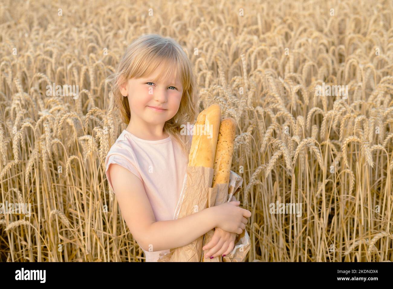 Happy little blonde girl holding a french bread baguette in a wheat