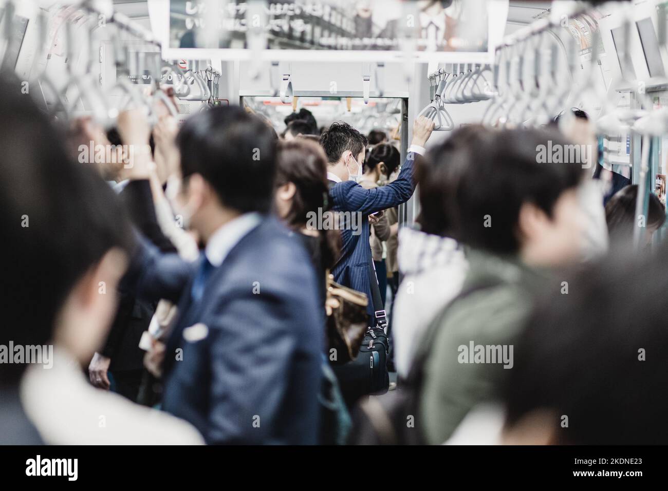 Passengers traveling by Tokyo metro. Business people commuting to work by public transport in rush hour. Shallow depth of field photo. Horizontal composition. Stock Photo