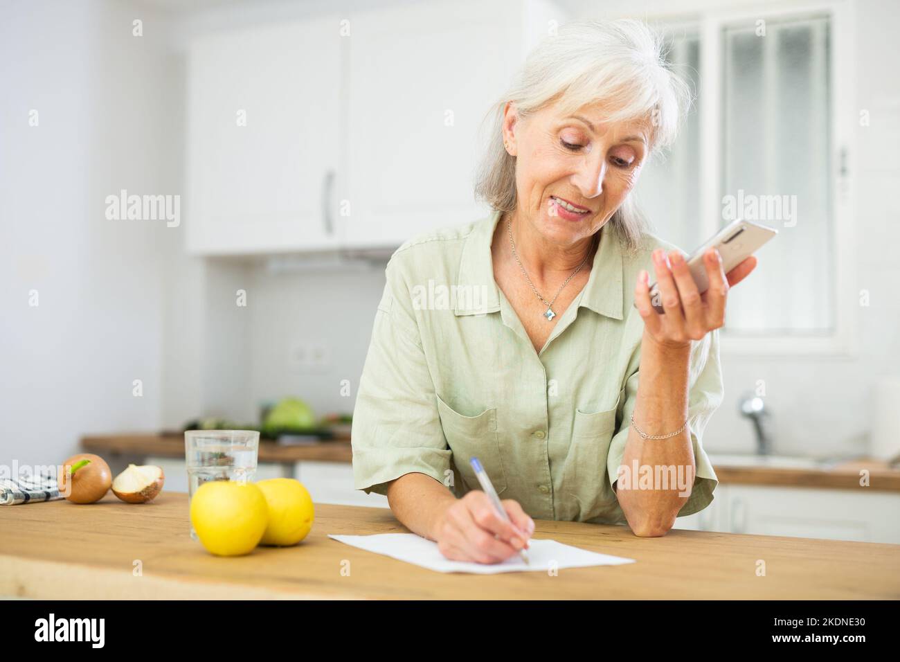 Positive senior woman talking on phone and making notes Stock Photo - Alamy