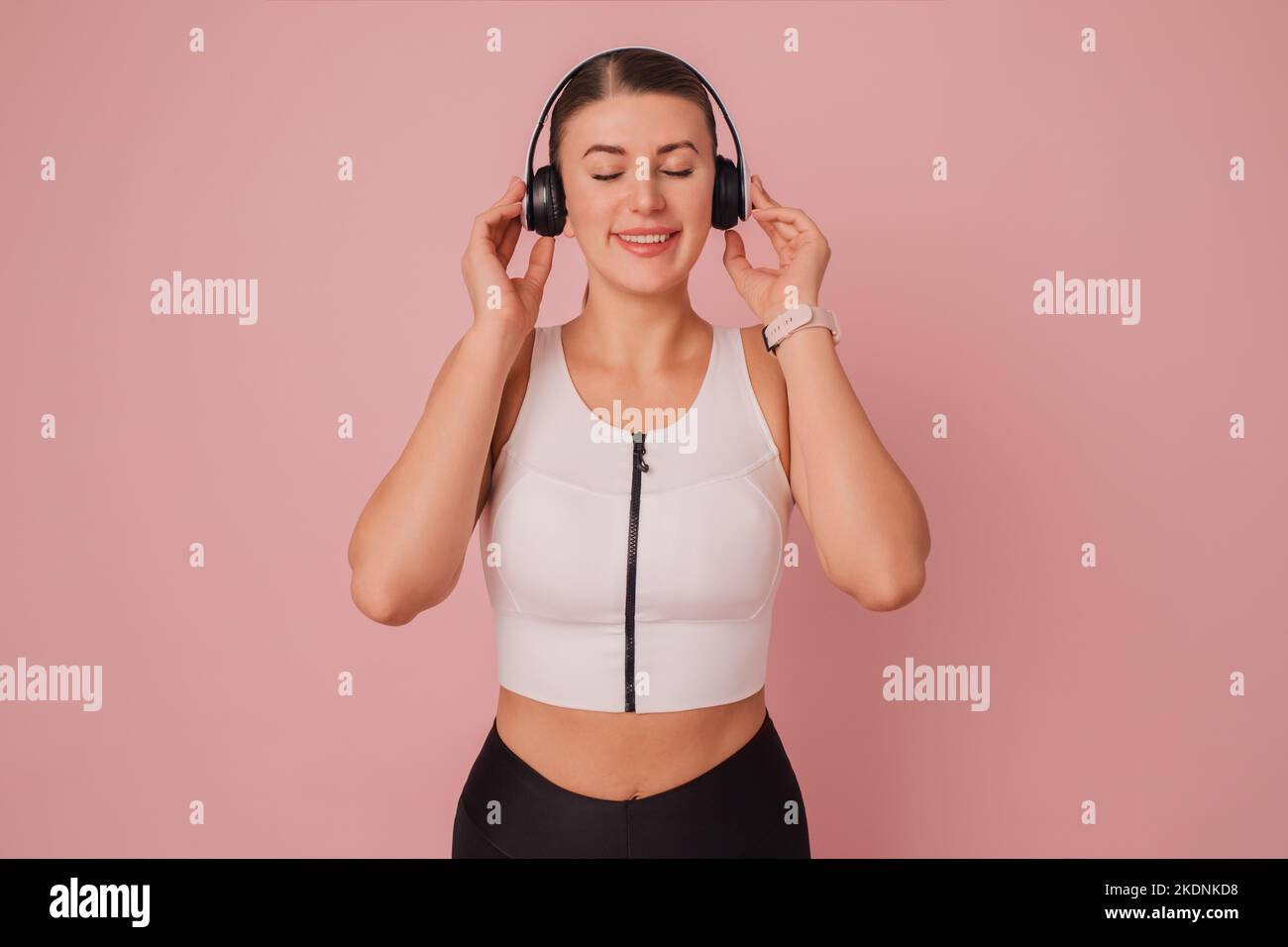 Happy woman in headphones. Relaxing and leisure time. Fitness girl with closed eyes in white headphones against pink background Stock Photo