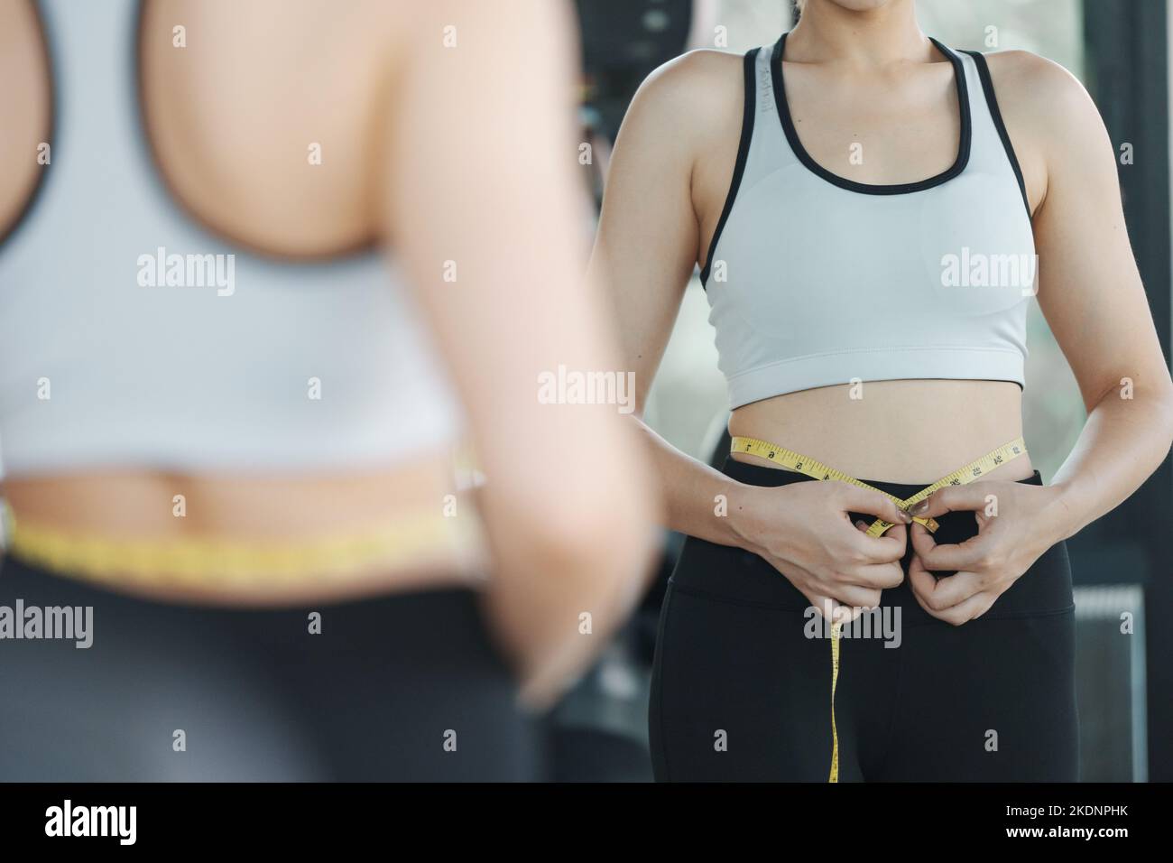 Young woman measuring her waist by measure tape at the gym. Stock Photo