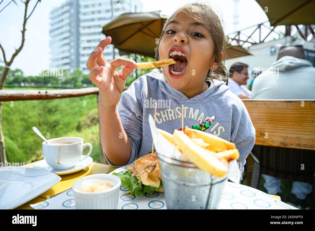 little girl has breakfast in a cafe, eats hamburger and french fries, drinks chocolate Stock Photo