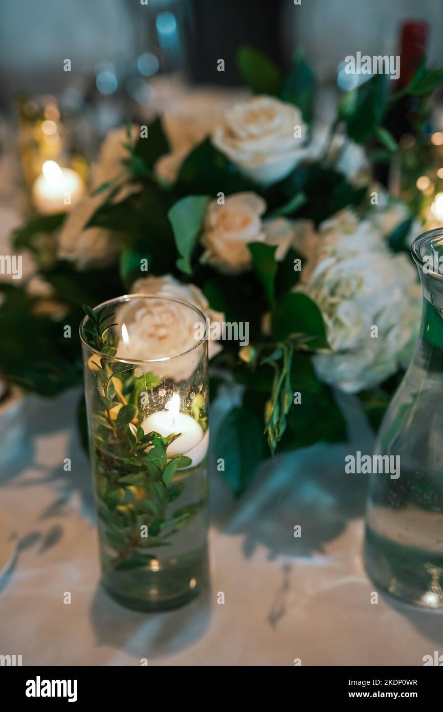 candle inside a glass vase in front of a center piece on a banquet hall table Stock Photo